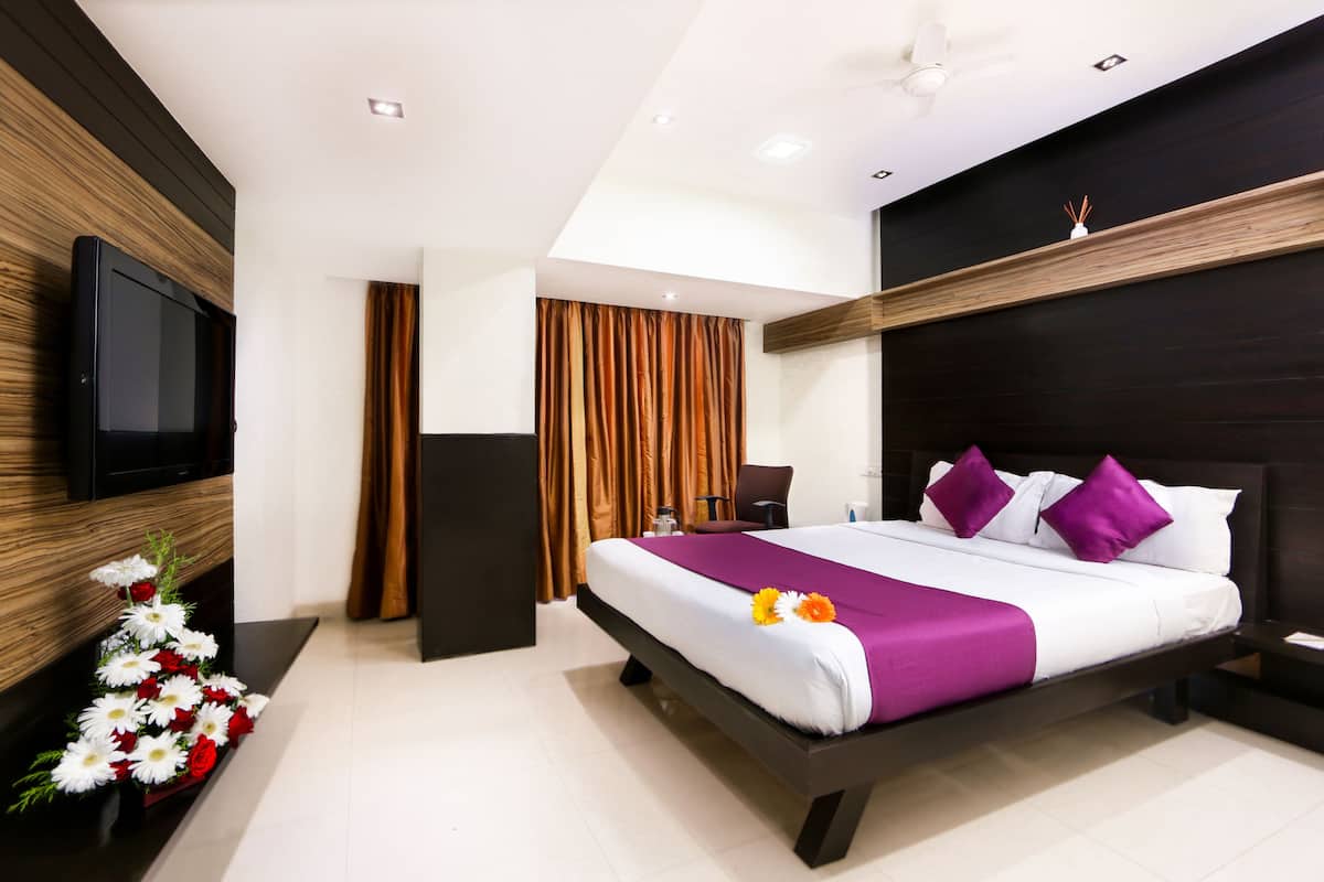 A modern hotel room with a large bed, a flat-screen TV, a wooden accent wall, and a ceiling fan.