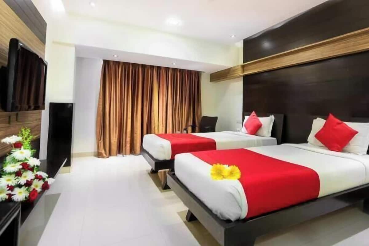 A hotel room with two beds, a TV, a desk, and a window with curtains.