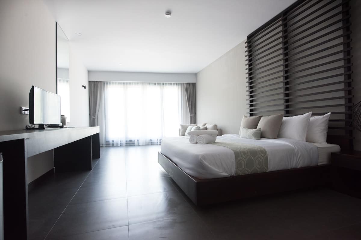 A modern hotel room with a large bed, a bedside table, a flat-screen TV, and a large window with curtains.