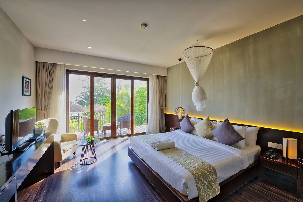 A modern hotel room with a large bed, a TV, a desk, and a view of the outdoors.
