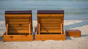 Two wooden beach chairs with a dark top, placed on a sandy beach with the ocean in the background. - Ren Resort (Sihanoukville)