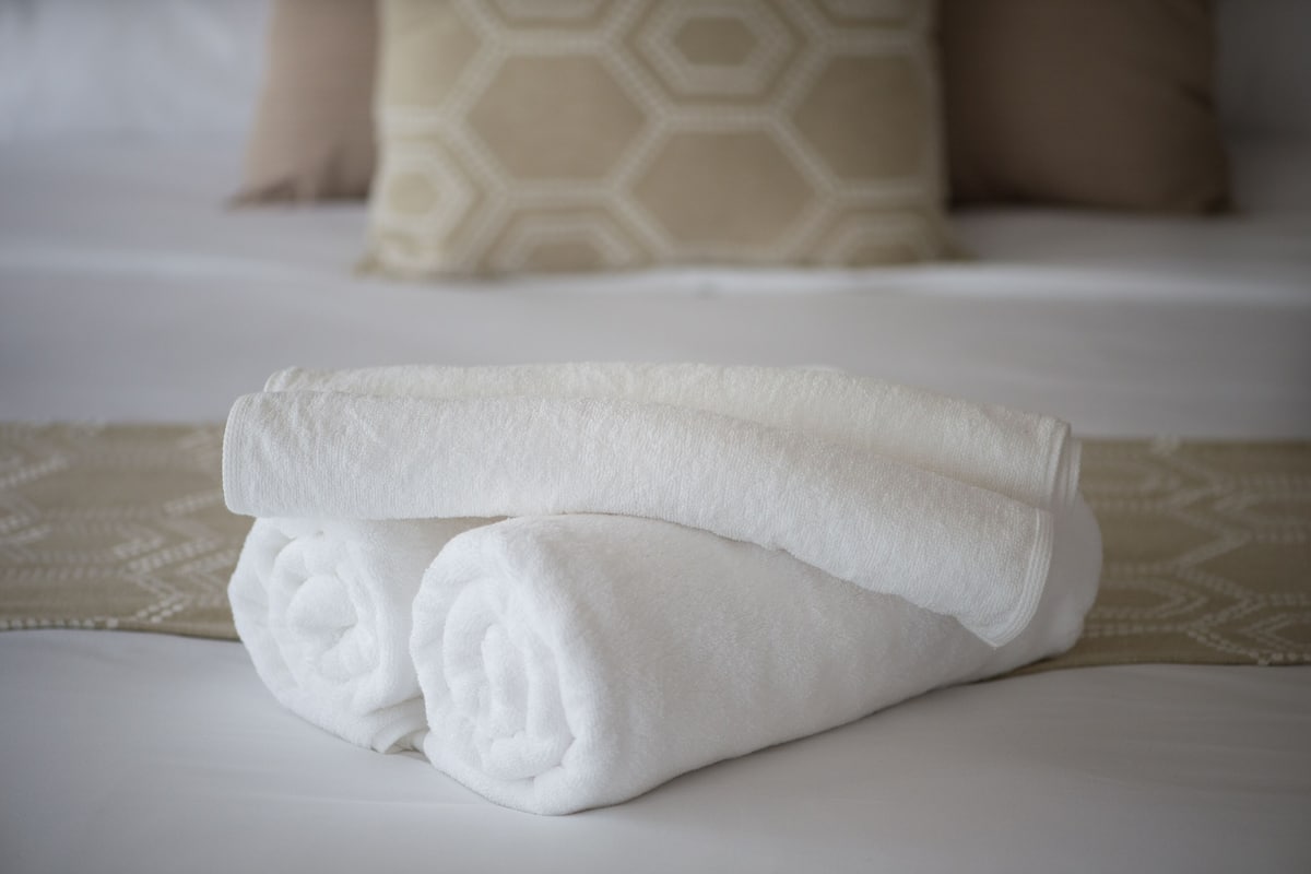 A neatly folded white towel on a bed with a patterned bedspread.