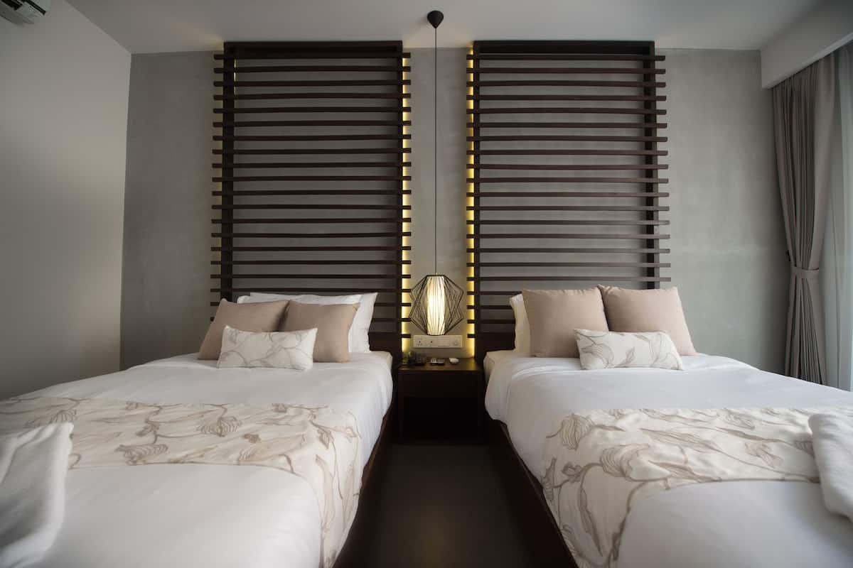 A hotel room with two beds, a modern light fixture, and a neutral color scheme.