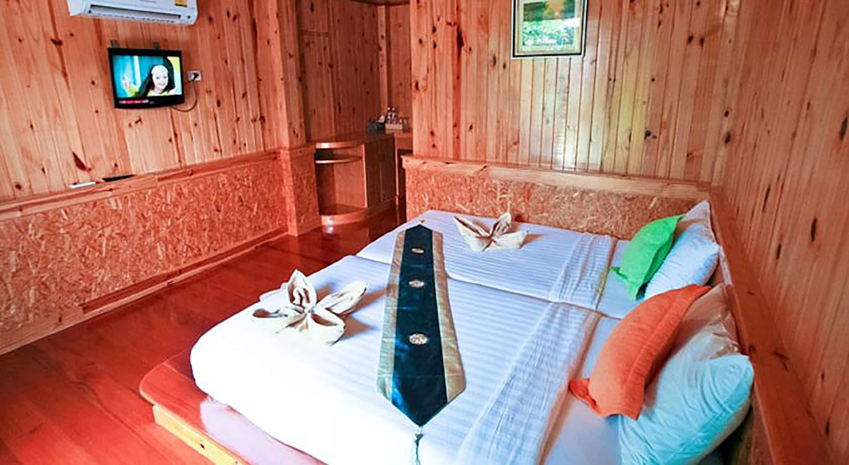 Una habitación de madera con una cama, un televisor y un cuadro en la pared.