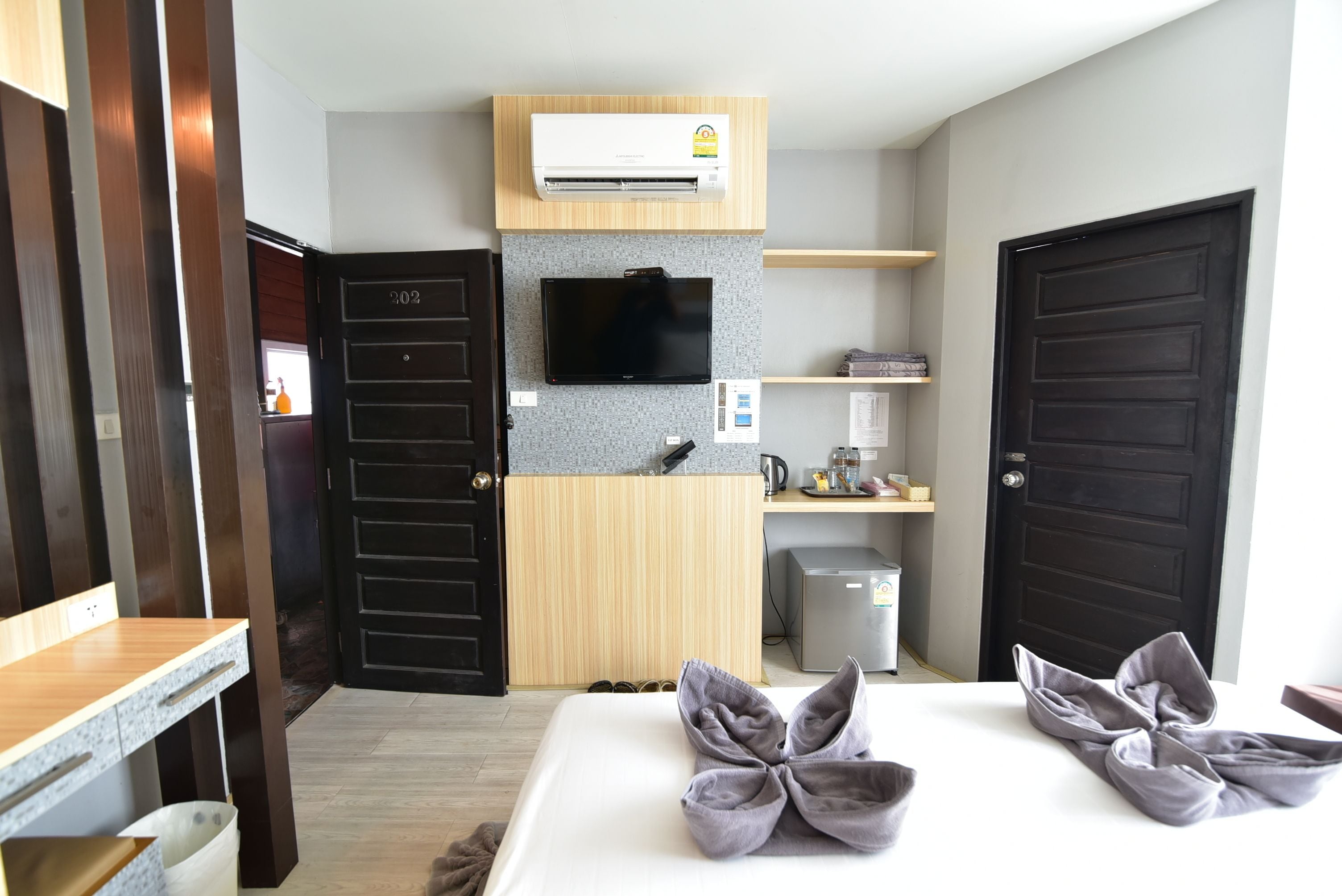 Une chambre d’hôtel avec un lit, un téléviseur fixé au mur, une petite kitchenette et une porte.