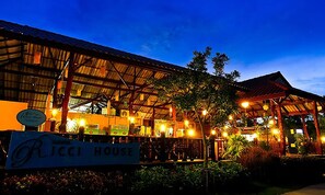 A rustic building with a sign reading "RICCI HOUSE" and a covered outdoor area with lights.