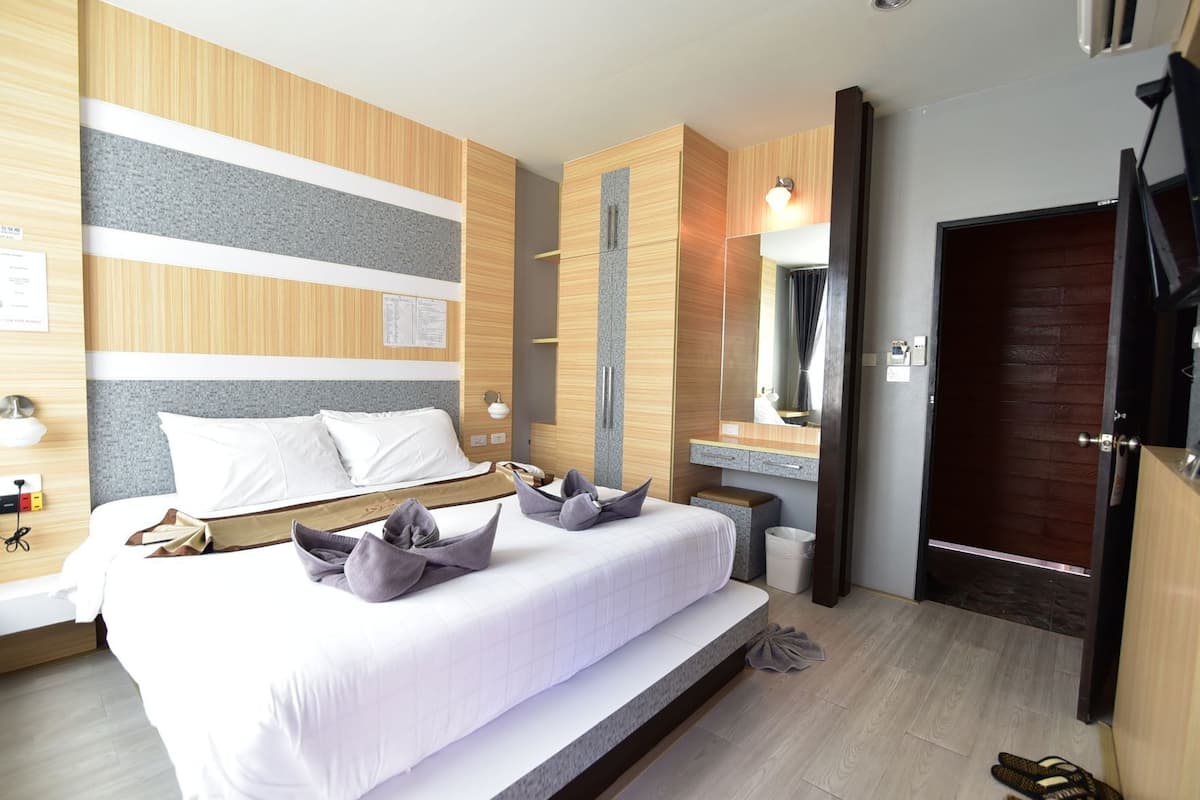Una habitación de hotel con una cama, un espejo, un armario de madera, una mesita y una puerta.