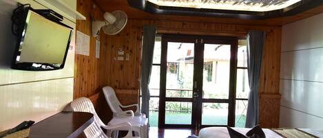 A room with a wooden ceiling, a flat-screen TV, a desk with a chair, a bed, and a view of the outside.