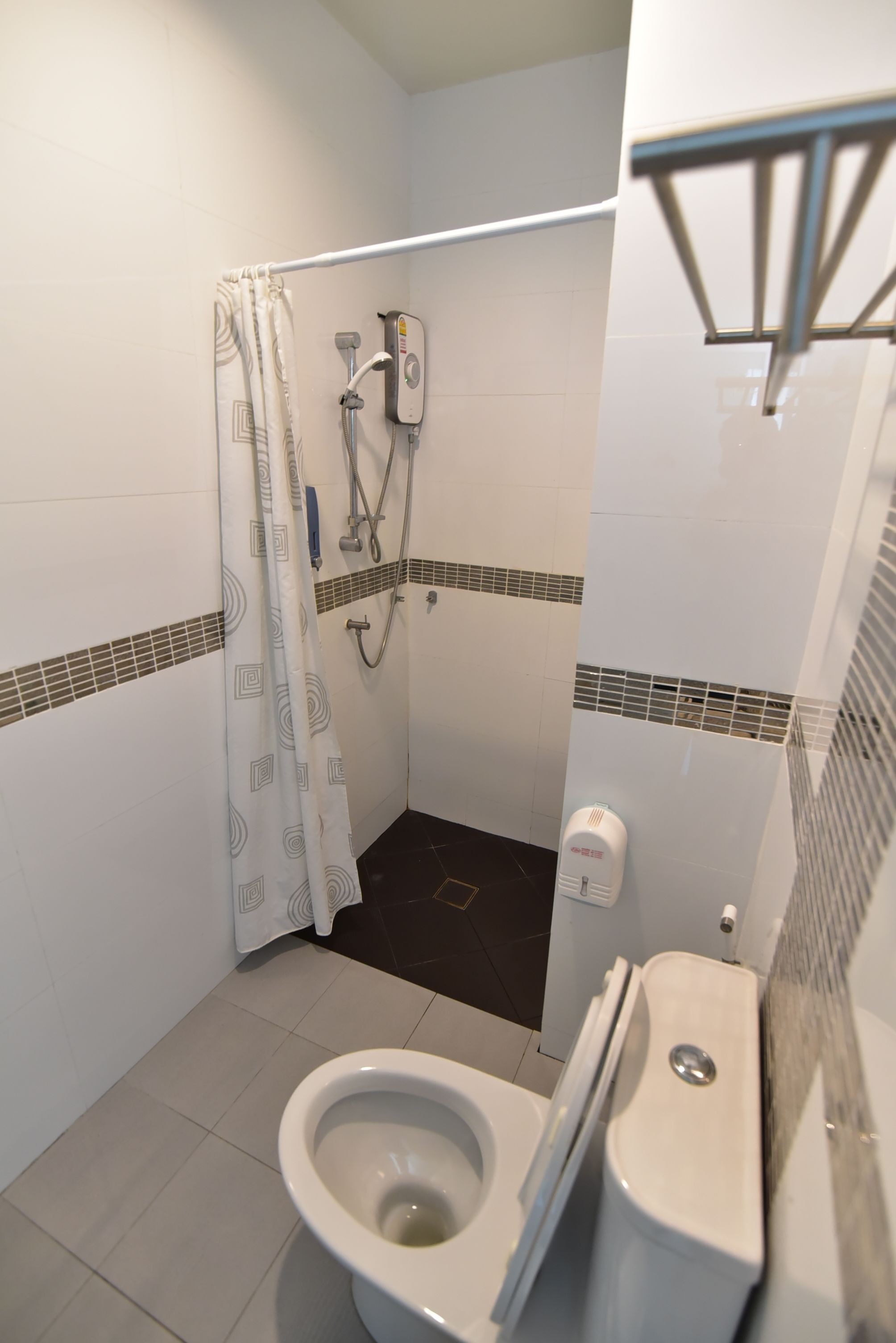 Une petite salle de bain avec douche, toilettes et sèche-mains.