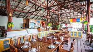 A restaurant with wooden tables and chairs, a counter with a menu, and a high ceiling with metal beams. - Ricci House Resort (Koh Lipe)
