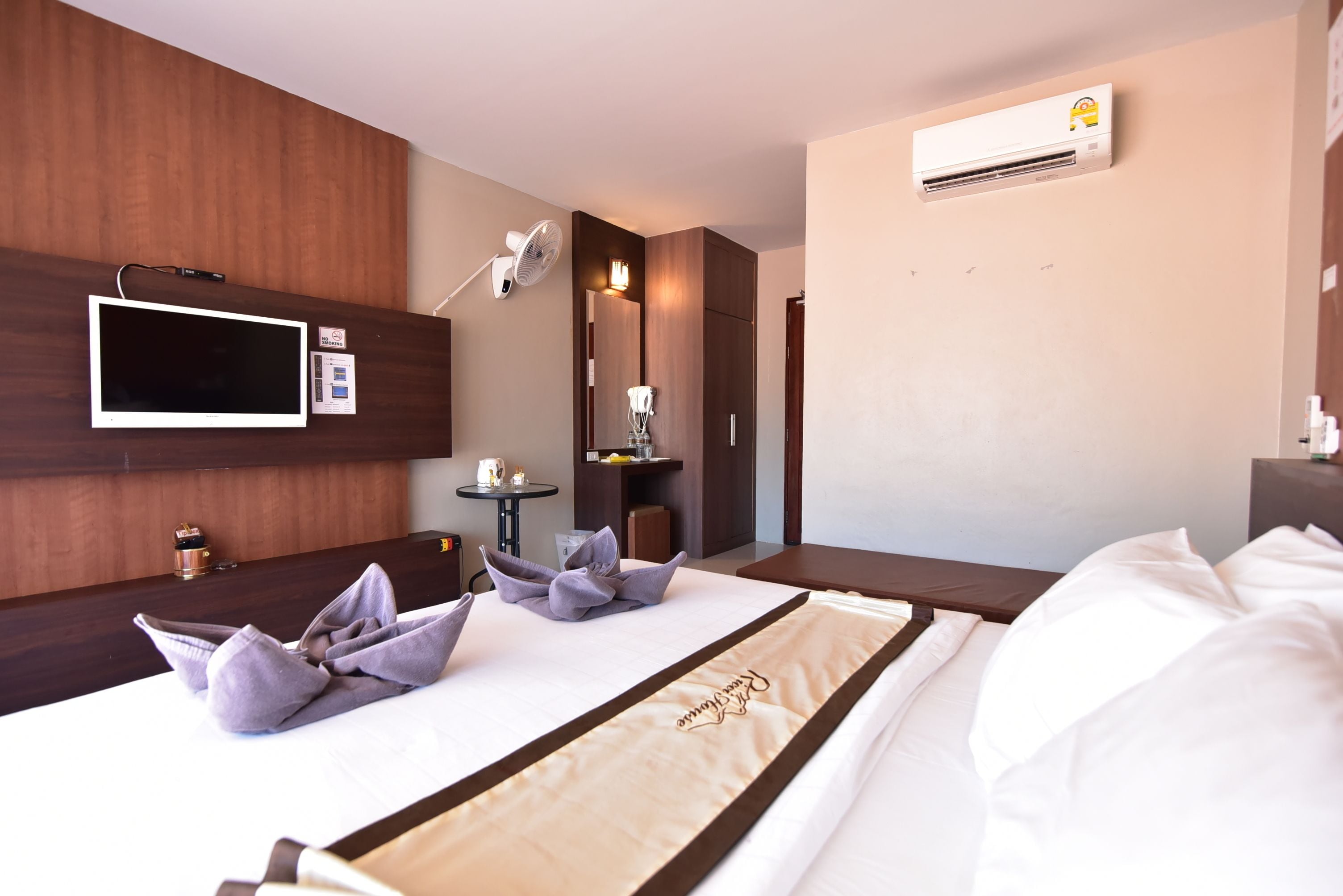 Habitación de hotel con cama, televisor de pantalla plana, escritorio con lámpara y equipo de aire acondicionado.