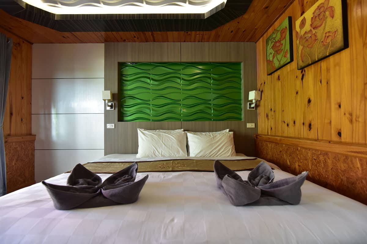Una habitación de hotel con una cama grande, un cabecero verde con textura y dos lámparas fijadas a la pared.