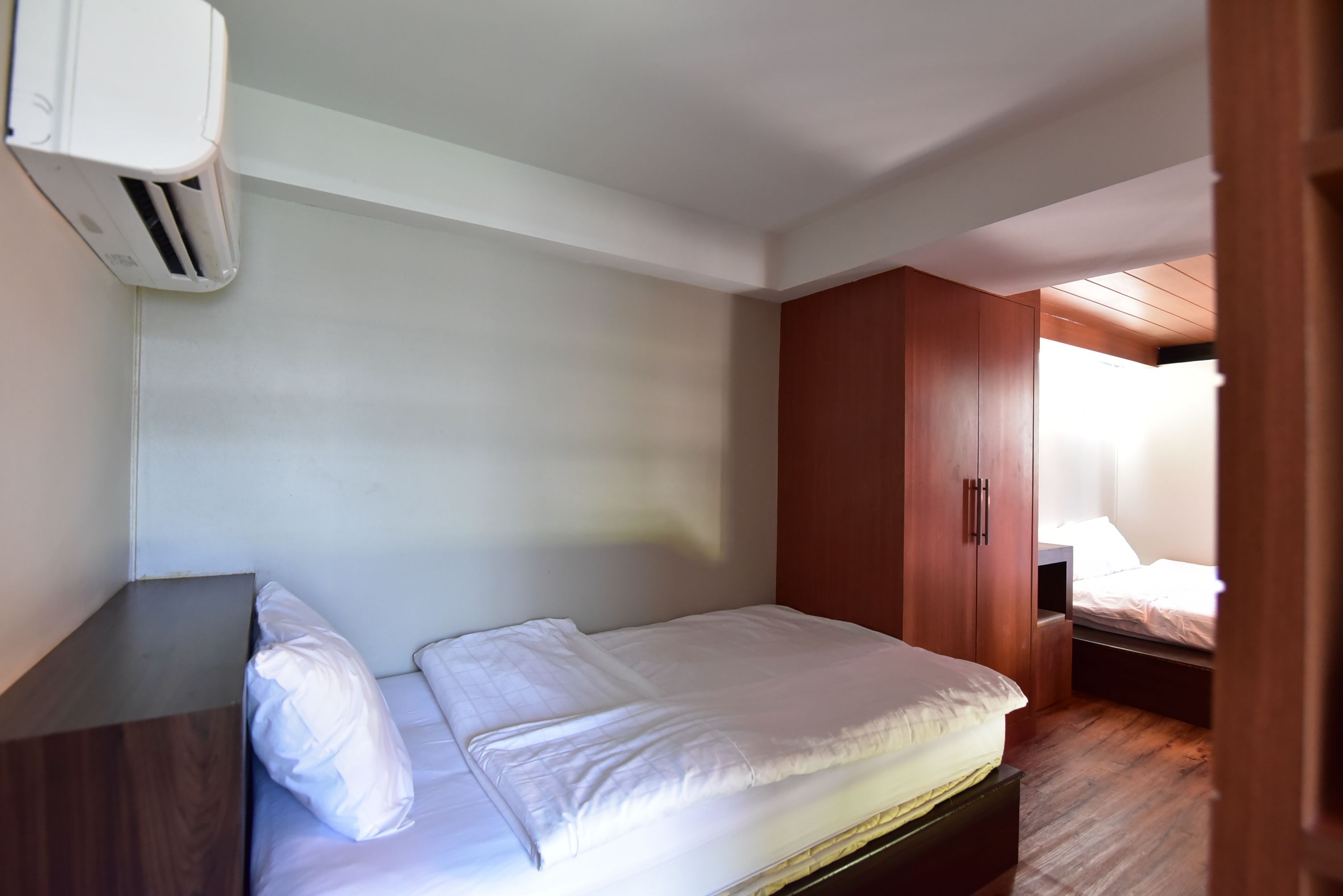 Une chambre à coucher avec un lit, une armoire en bois et un climatiseur fixé au mur.