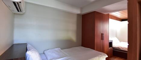 A bedroom with a bed, a wooden wardrobe, and a wall-mounted air conditioner.