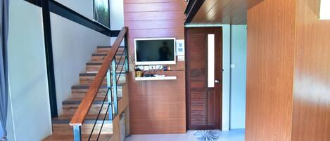A modern interior with a wooden staircase, a mounted TV, and a door leading to another room.