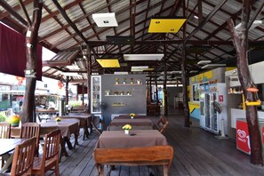 An indoor dining area with wooden tables and chairs, a counter with a menu, and a refrigerated display case.