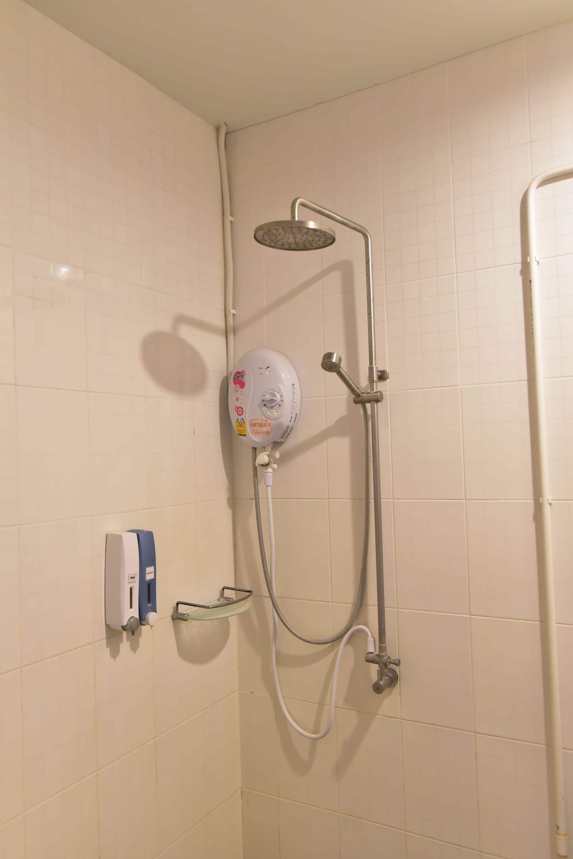 Een douche met een handdouche, een bedieningspaneel aan de muur en een glazen plank.