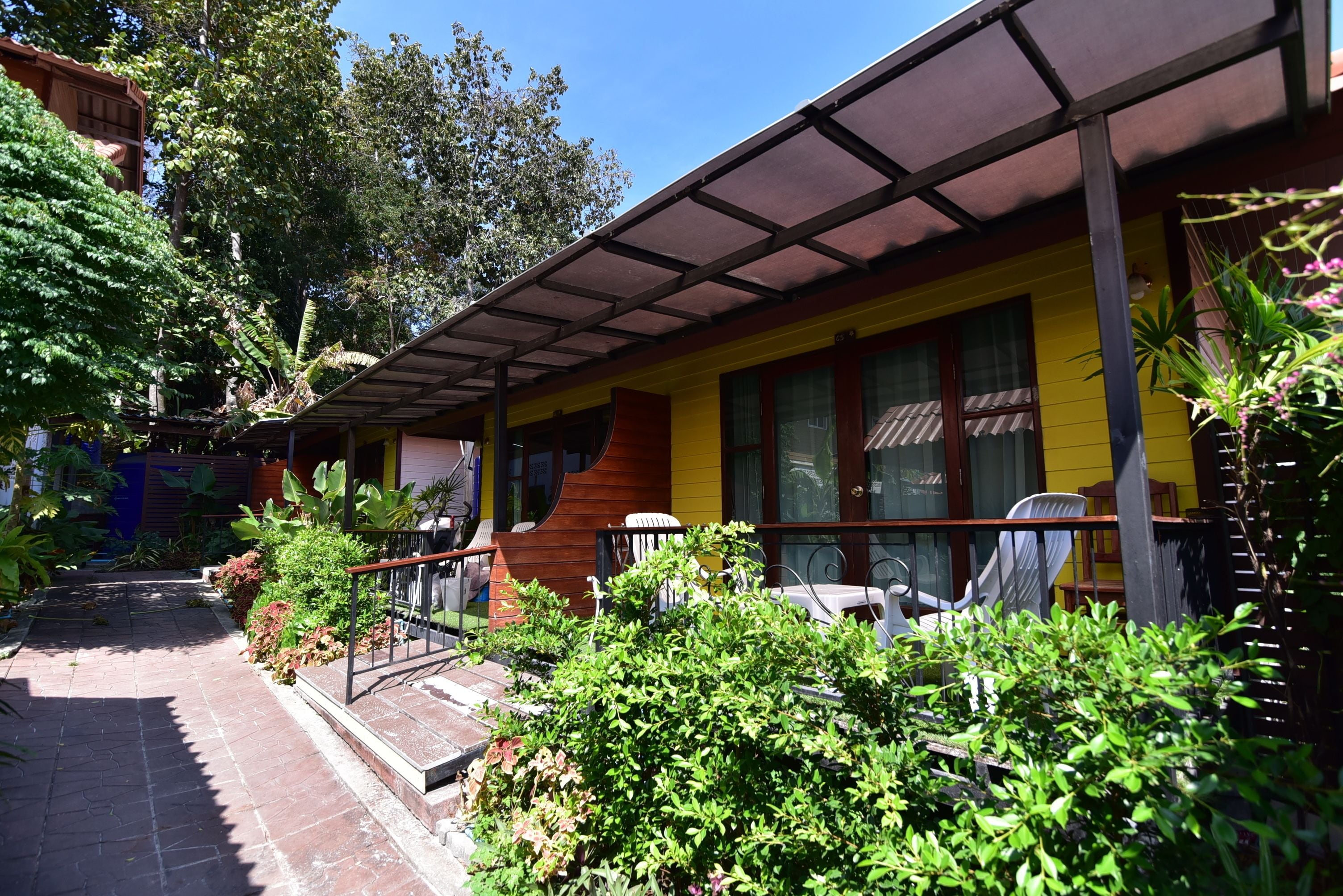 A two-story building with a yellow facade, a covered porch with chairs, and a brick pathway leading to the entrance.