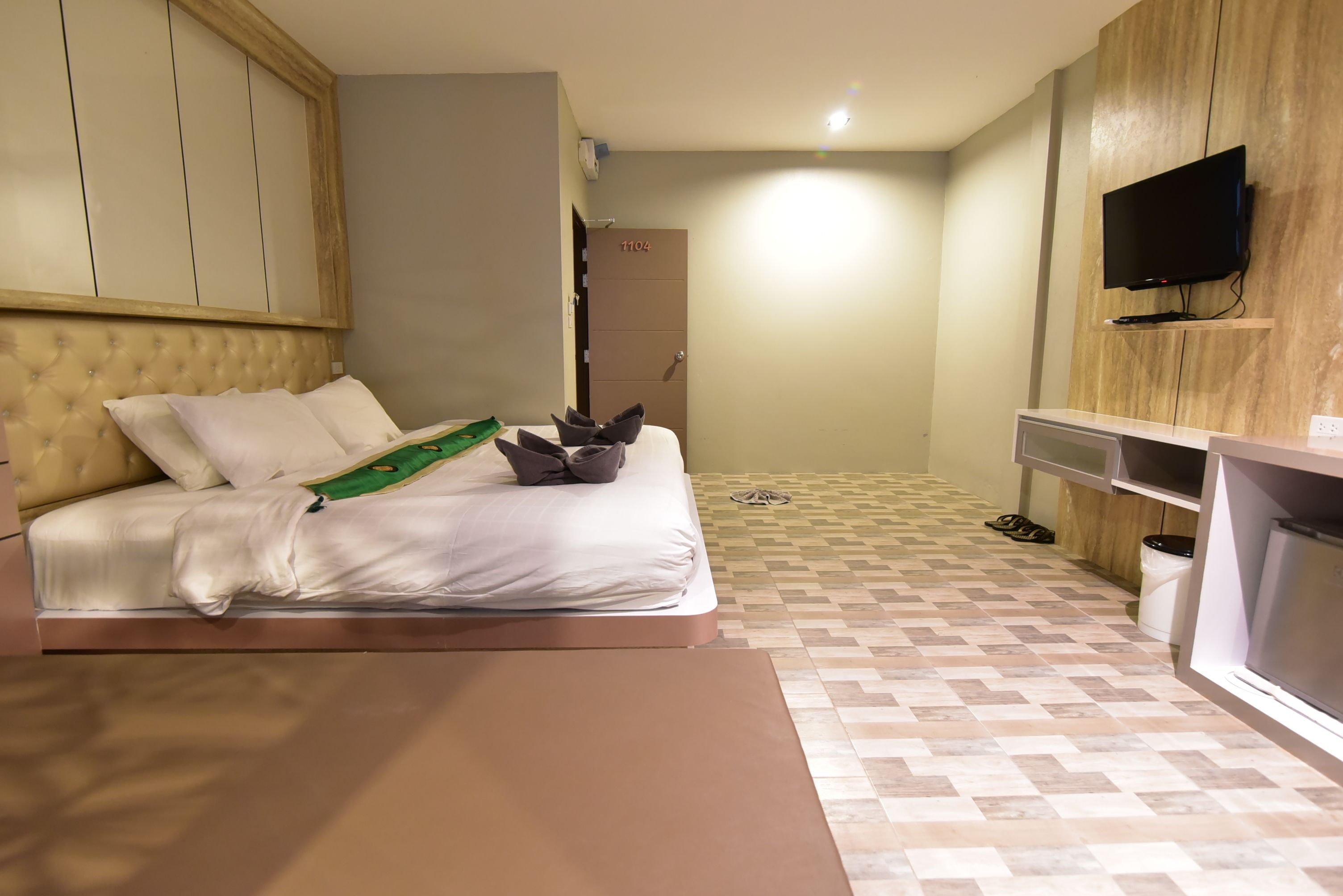 Una habitación de hotel con una cama, un televisor montado en la pared y una pequeña zona de kitchenette.
