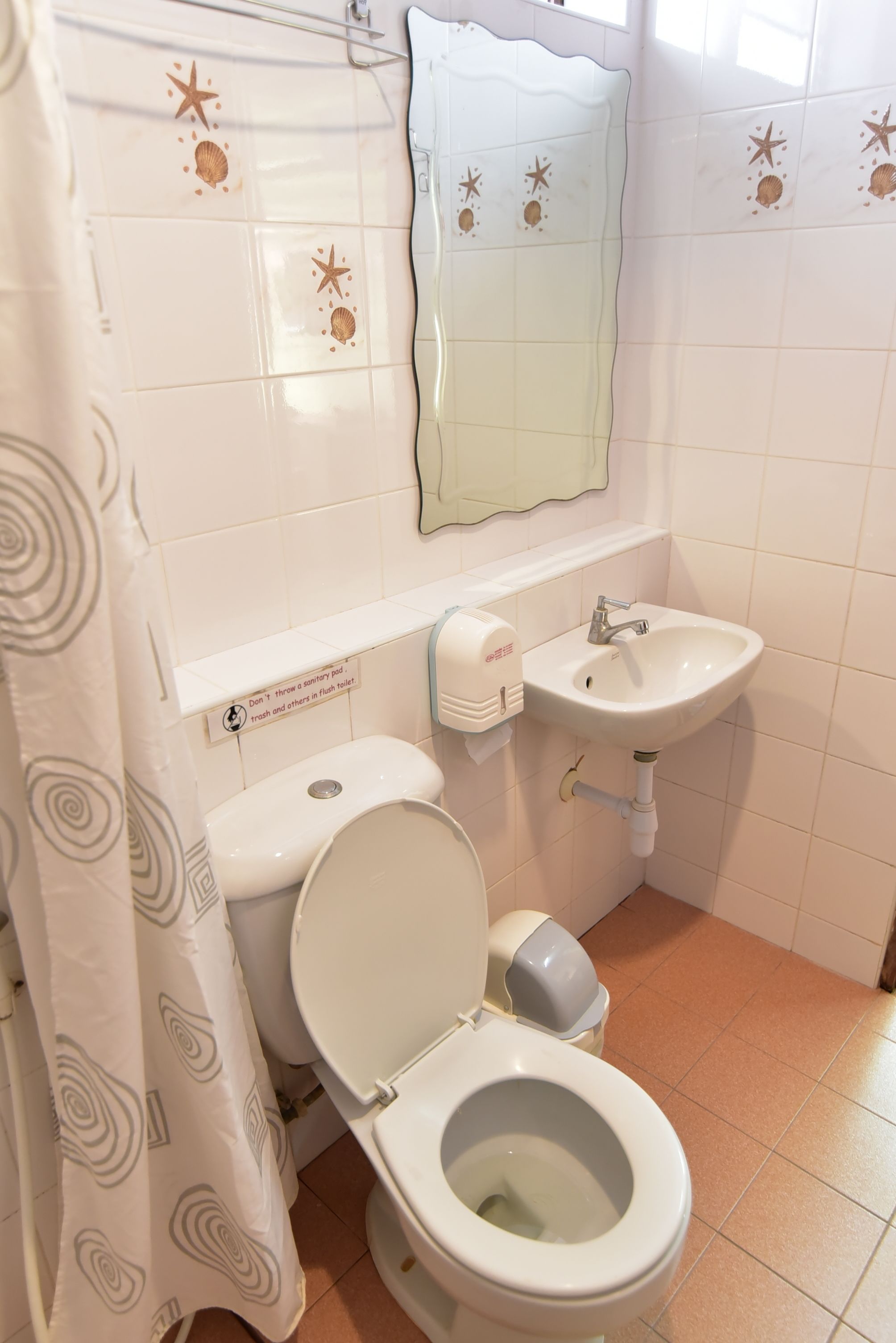 A bathroom with a toilet, sink, and a mirror. There is a sign on the wall next to the toilet.