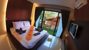 A hotel room with a bed, a TV, and a view of a balcony with a fence and greenery. - Ricci House Resort (Koh Lipe)