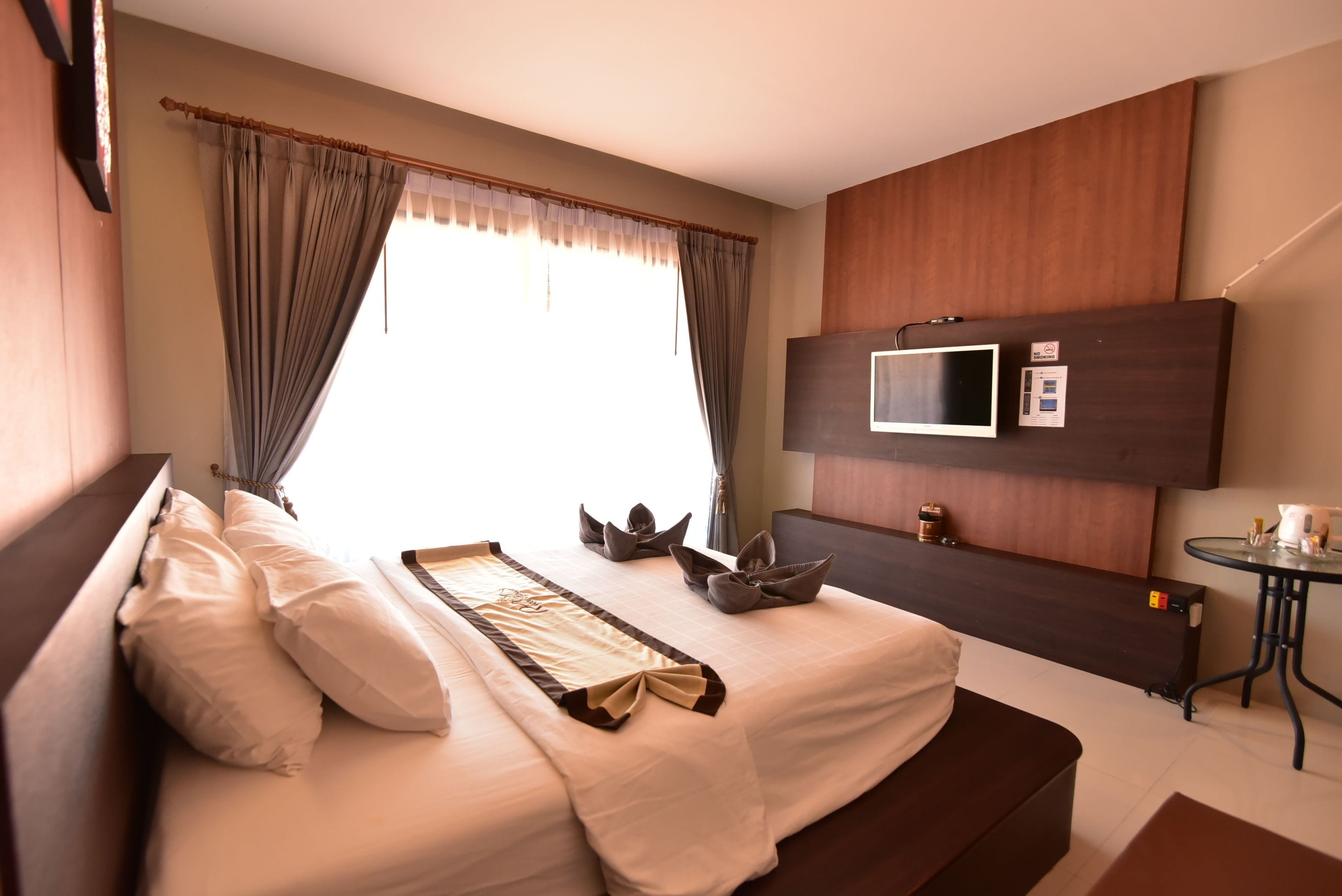 A hotel room with a large bed, a flat-screen TV mounted on the wall, and a small table with a kettle.