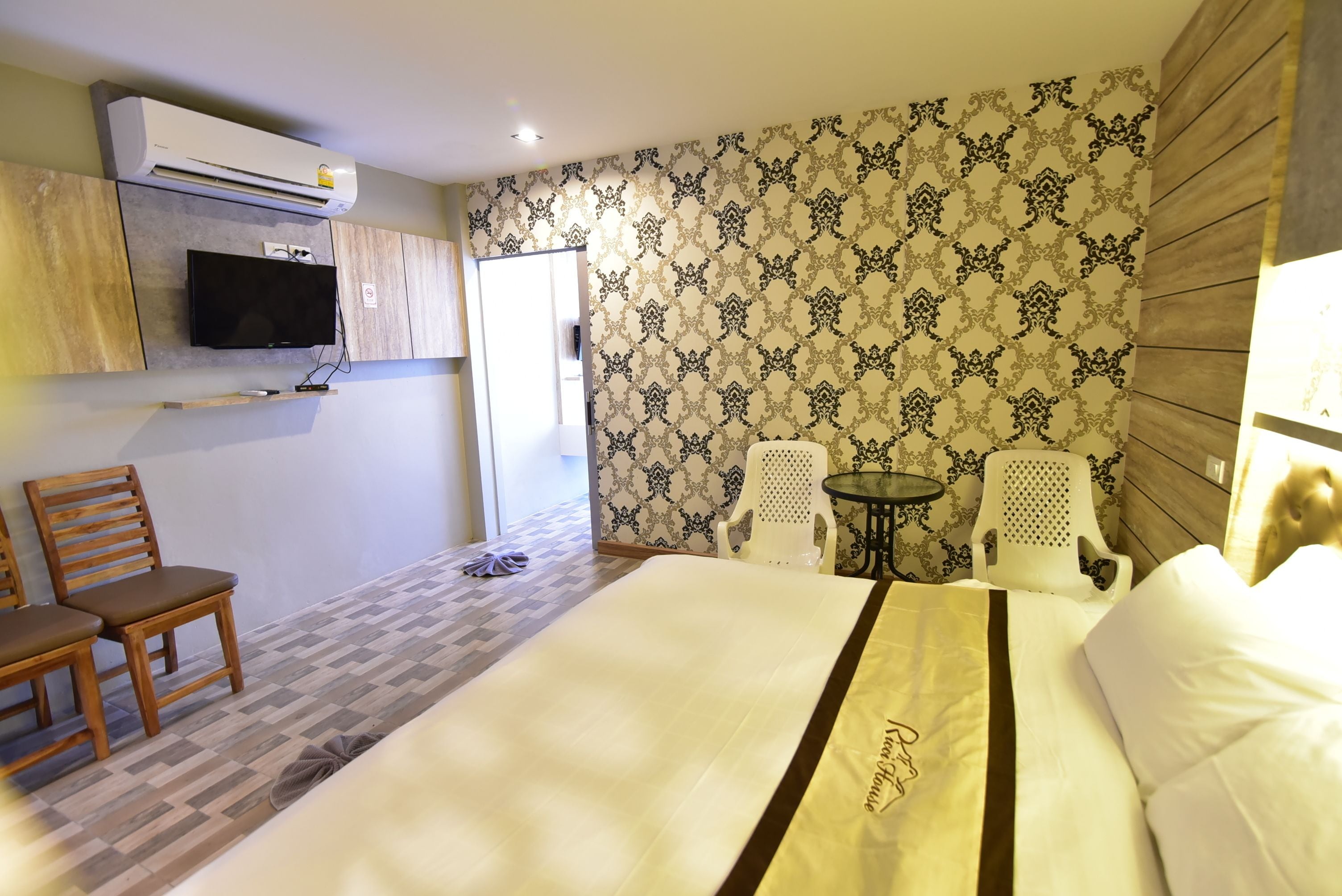 A hotel room with a bed, a TV mounted on the wall, two chairs, and a small table.