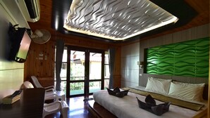 A modern hotel room with a large bed, a flat-screen TV, a ceiling fan, and a view of the outdoors. - Ricci House Resort (Koh Lipe)