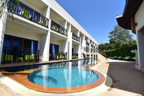 A hotel with a swimming pool, multiple balconies, and a clear blue sky.