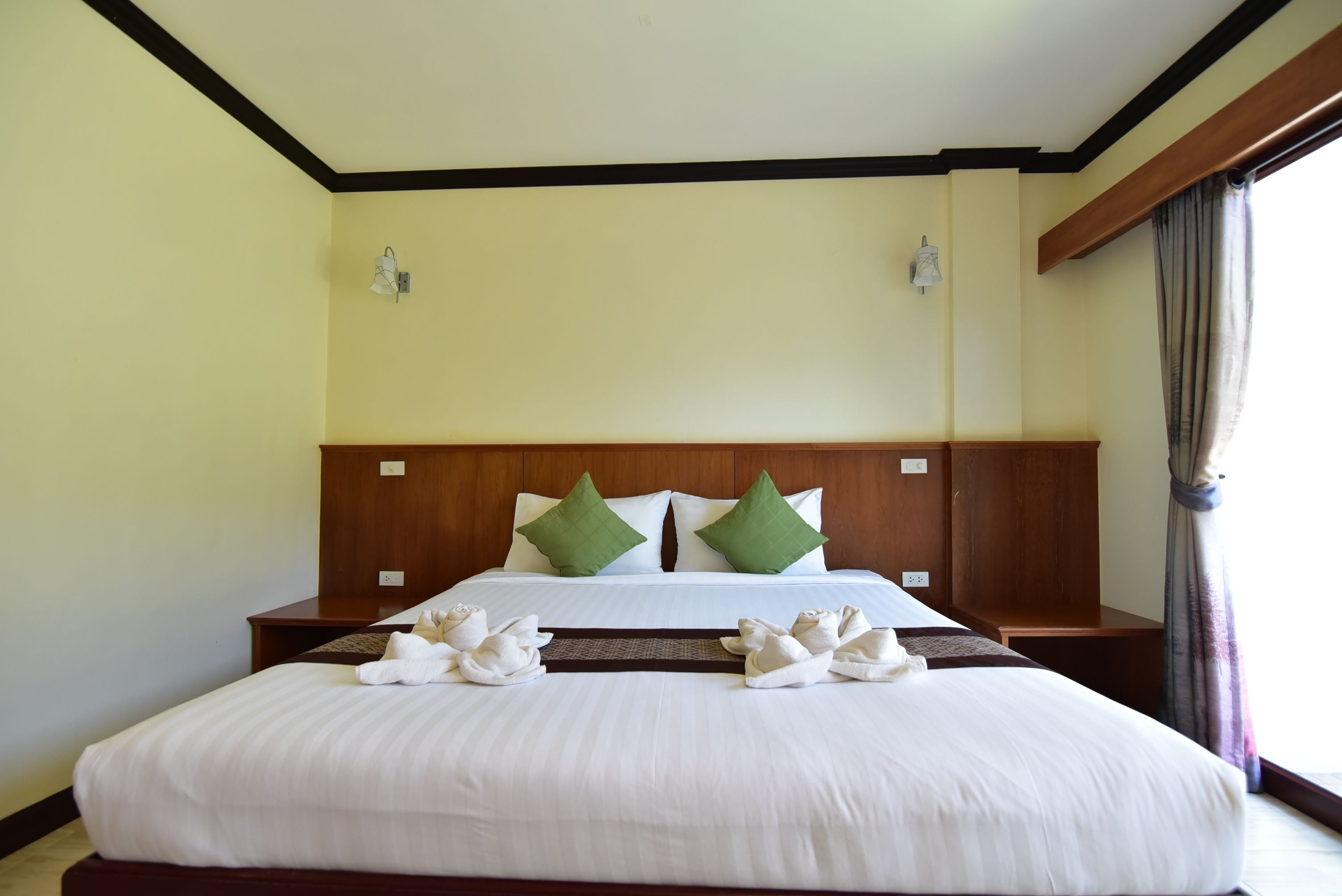 A neatly made bed with white linens, two green pillows, and a wooden headboard.