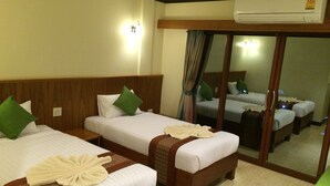 Habitación de hotel con dos camas, cada una con sábanas blancas y almohadas verdes, un cabecero de madera, una mesita de noche y un espejo que refleja la habitación.