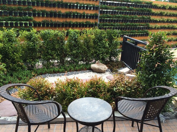 Un espace patio aménagé avec des meubles en osier et une petite table, entouré de plantes en pot disposées avec soin et d’un jardin de rochers.