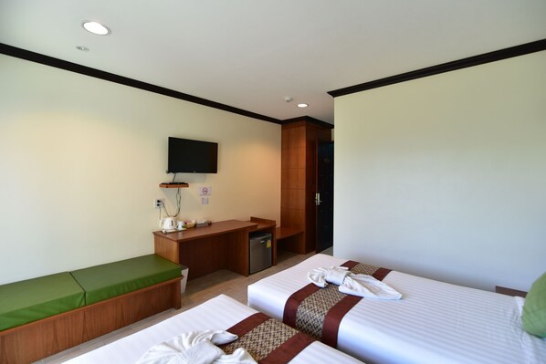 Habitación de hotel con dos camas, un escritorio, una kitchenette pequeña y un televisor en la pared.