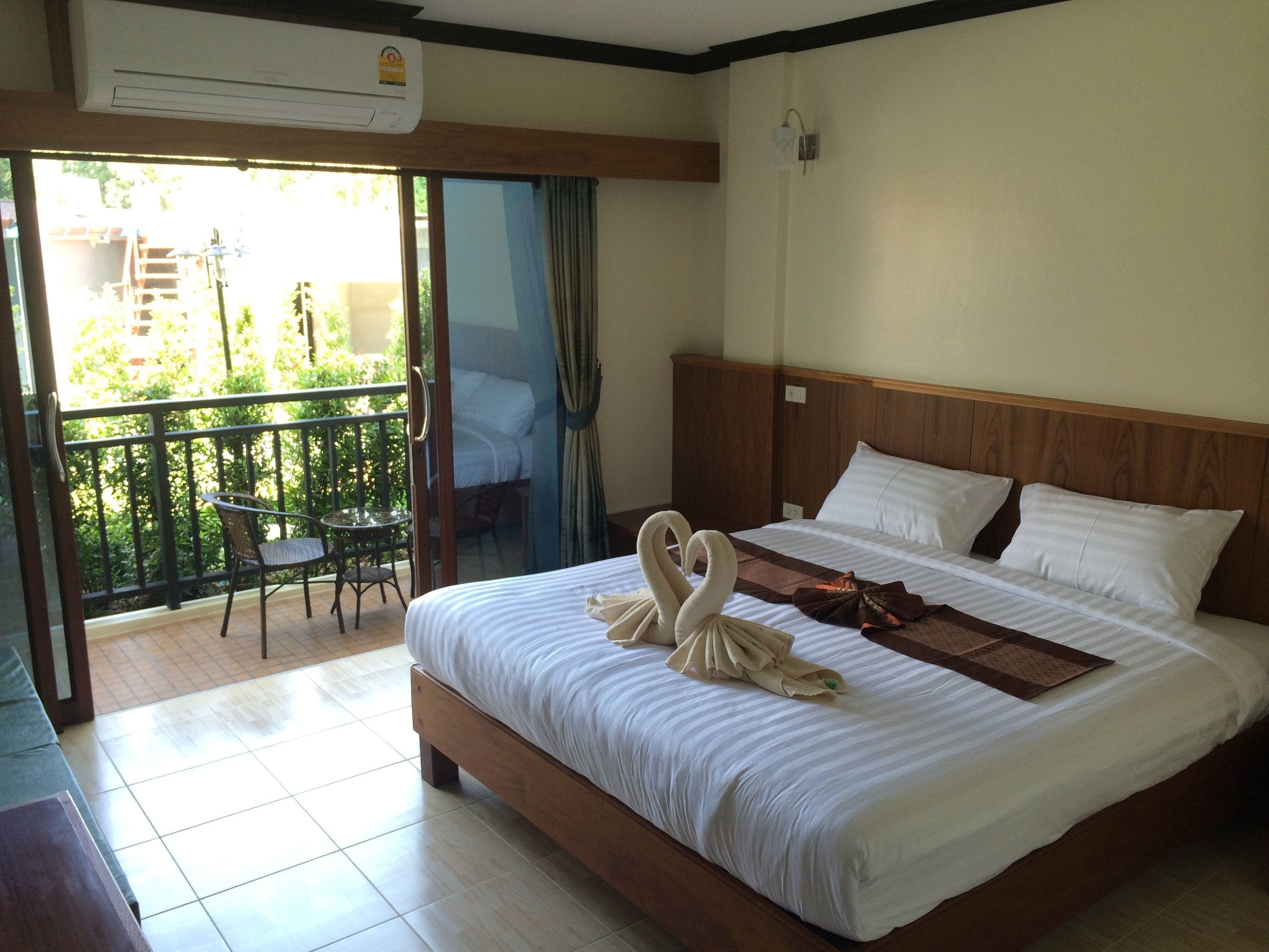 A hotel room with a bed, a balcony with a table and chairs, and an air conditioning unit.