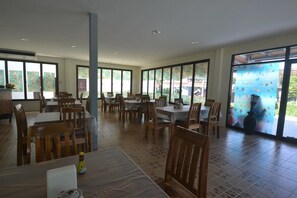 A spacious dining area with multiple tables and chairs, large windows, and a view of the outdoors.