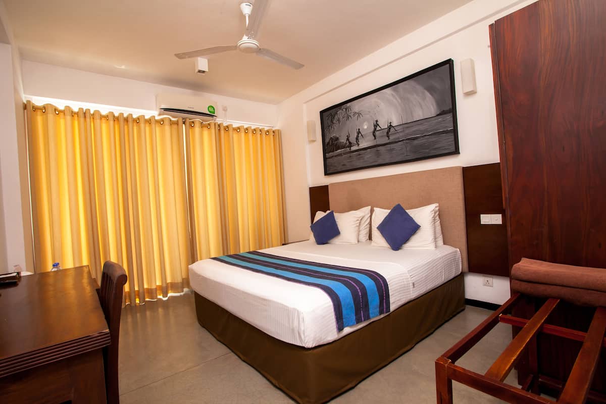 Habitación de hotel con cama, escritorio, silla, ventilador de techo y un cuadro en la pared.