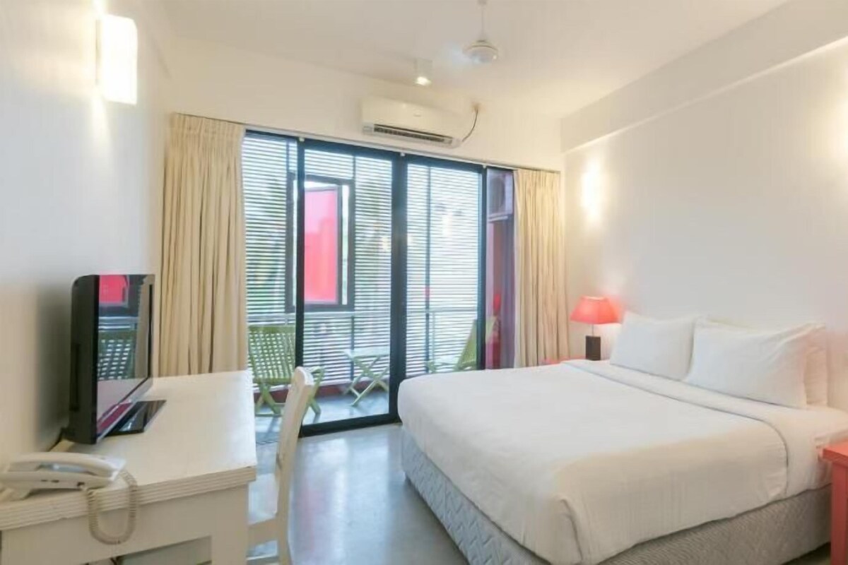 Una habitación de hotel con cama, escritorio, silla y balcón con cortinas.