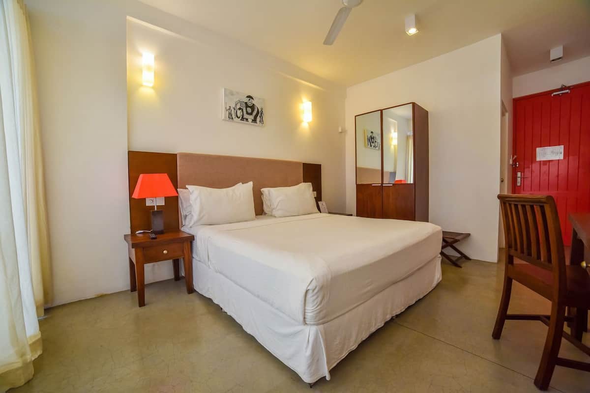 Una habitación de hotel con cama, mesita de noche, lámpara, silla y una puerta roja.
