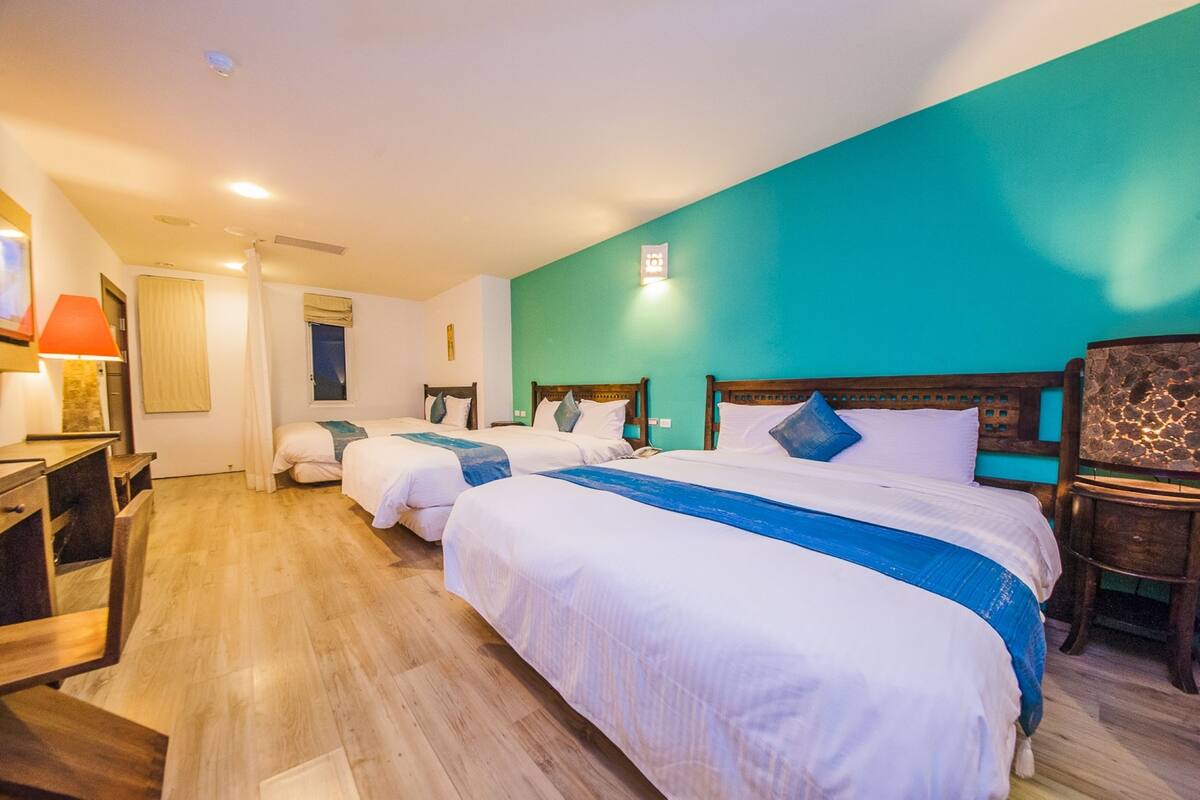 A hotel room with three beds, wooden furniture, and a teal accent wall.
