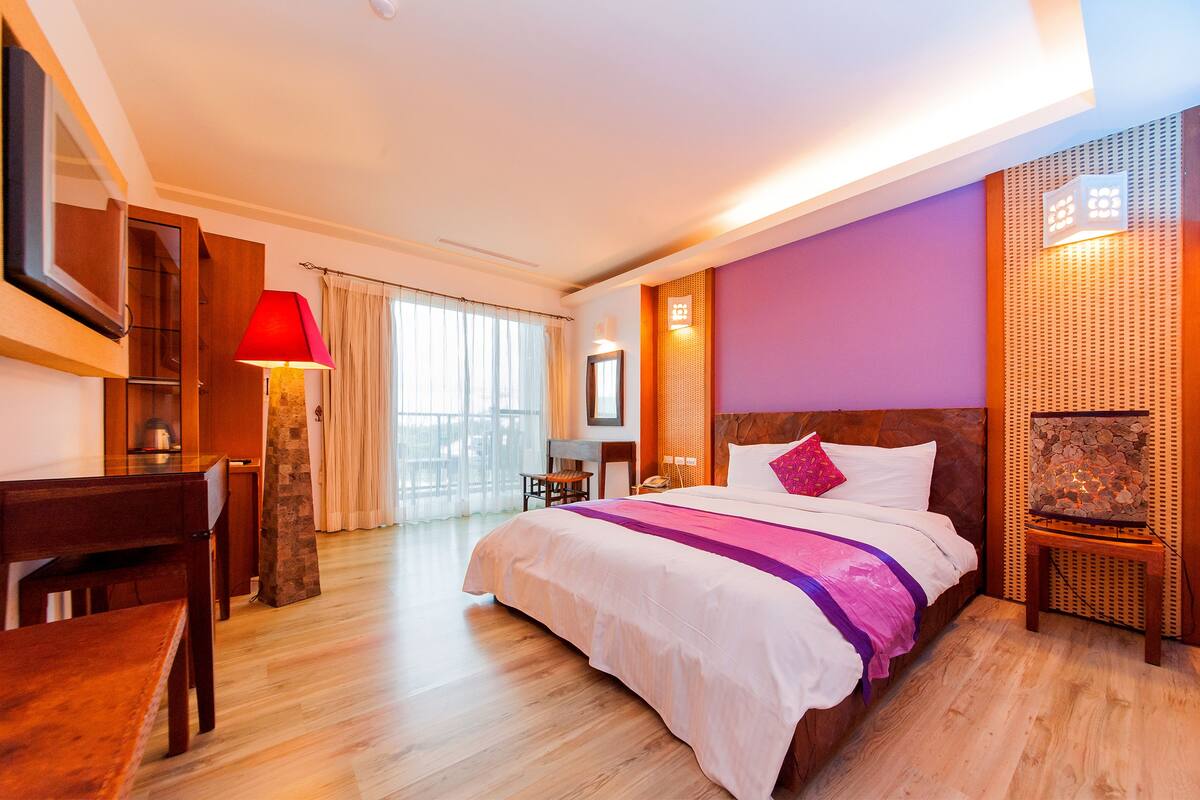 A hotel room with a large bed, a desk, a chair, a TV, and a window with curtains.