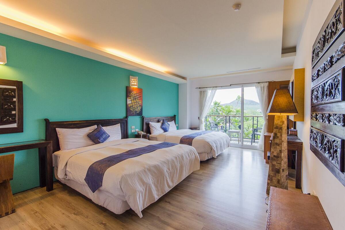 A hotel room with two beds, a balcony with a view, and a wooden floor.
