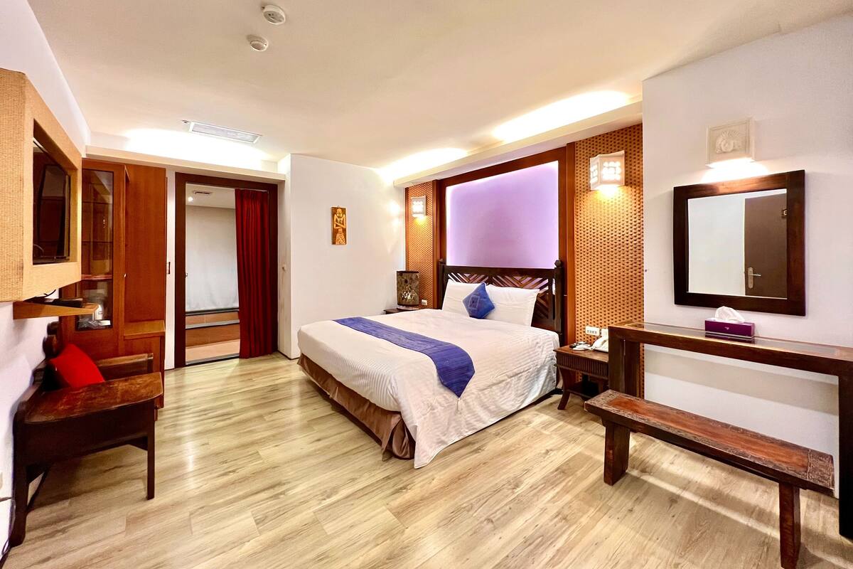 A hotel room with a bed, bedside table, bench, wooden floor, and a mirror on the wall.