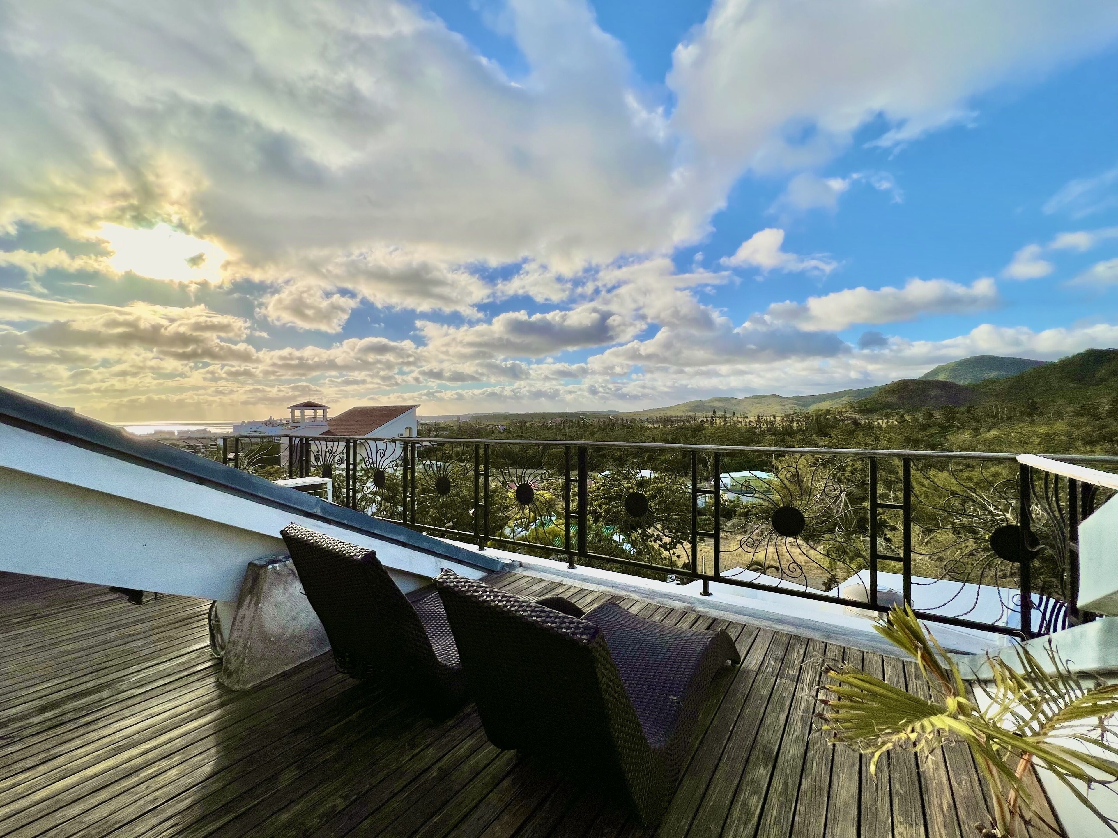A wooden deck with wicker furniture and a metal railing overlooking a mountainous landscape.
