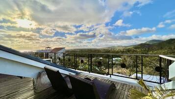A wooden deck with wicker furniture and a metal railing overlooking a mountainous landscape.