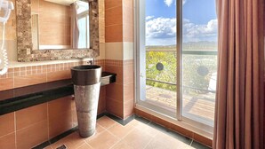 A bathroom with a stone wall, a sink, and a large window with a view of greenery and hills. - Seasons Bali Fashion Inn (Hengchun)