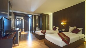 Habitación de hotel con dos camas, televisión, escritorio y baño visible a través de una puerta corrediza.