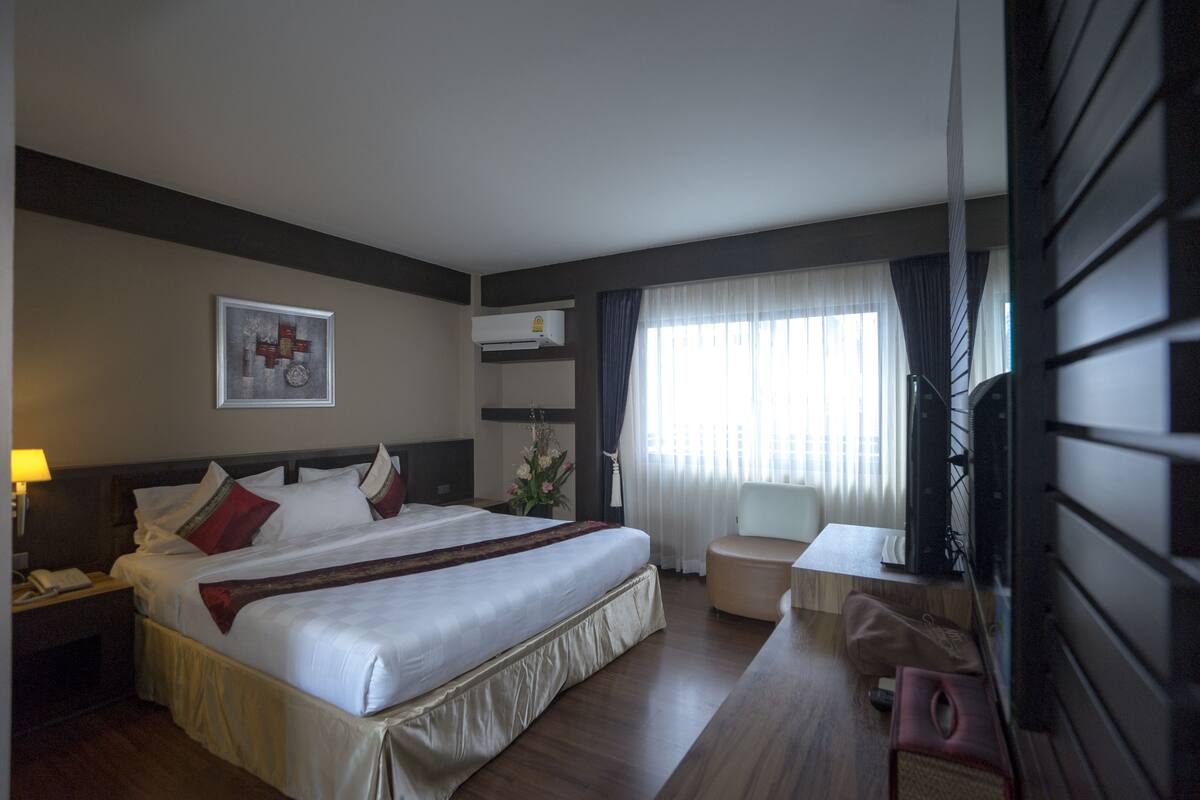 Een hotelkamer met een groot bed, nachtkastje, lamp en een televisie.