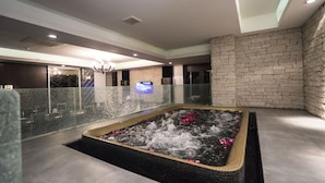 Un espacio de spa con hidromasaje, pared de piedra y barandilla de cristal.