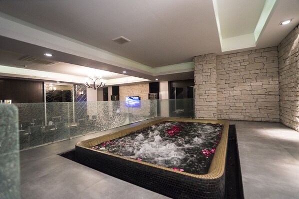 Un espacio de spa con hidromasaje, pared de piedra y barandilla de cristal.