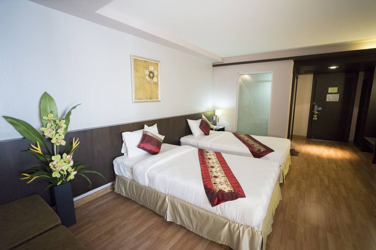 Een hotelkamer met twee bedden, een bloempot, een schilderij en een deur naar een andere kamer.